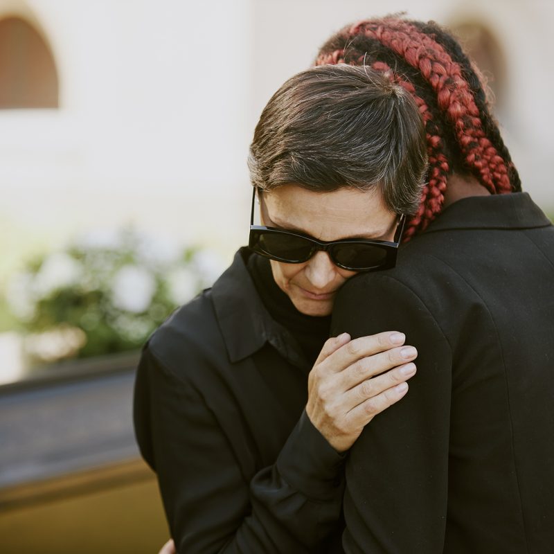 Senior Caucasian woman crying on her daughters shoulder at funeral