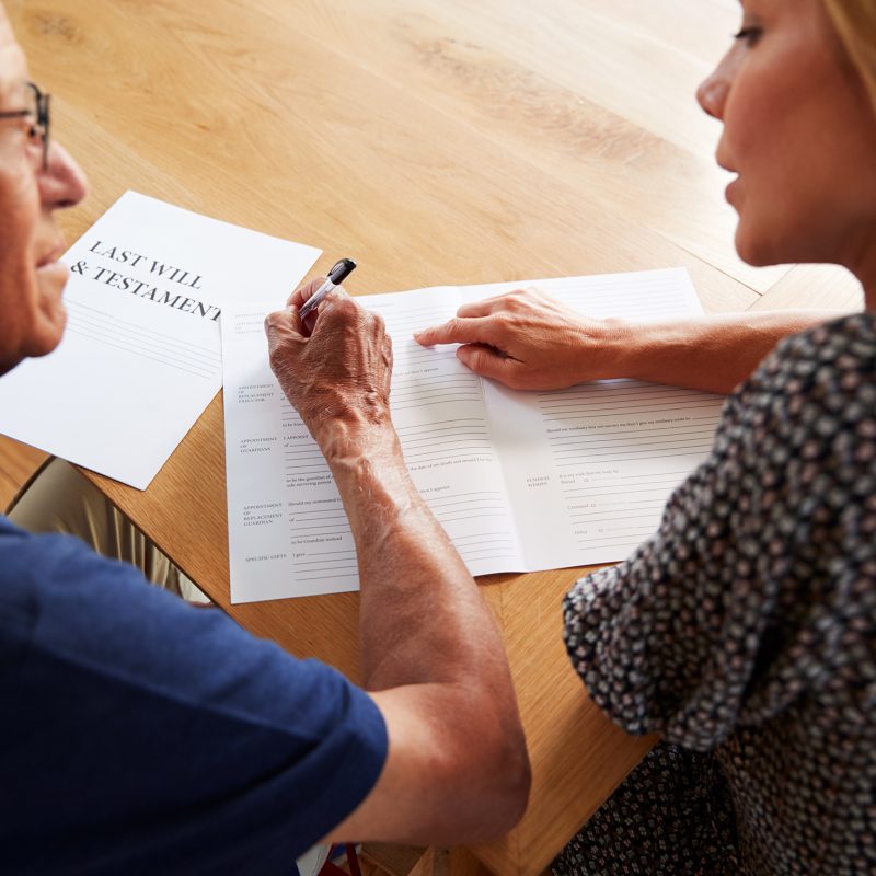 Woman Helping Senior Man To Complete Last Will And Testament At Home